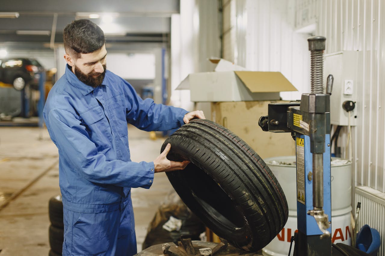 Mechanic in blue uniform examining a tire in an automotive garage.